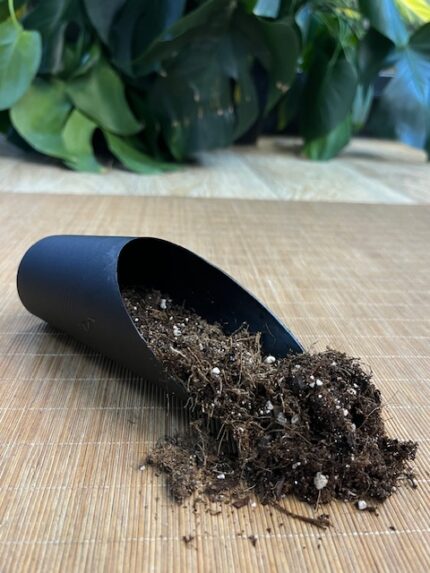 Zbliżenie na szarą lub zieloną plastikową łopatkę do nabierania podłoża, leżącą obok opakowania granulatu Lechuza PON. Łopatka ma wąski, wyprofilowany kształt i wygodny uchwyt.